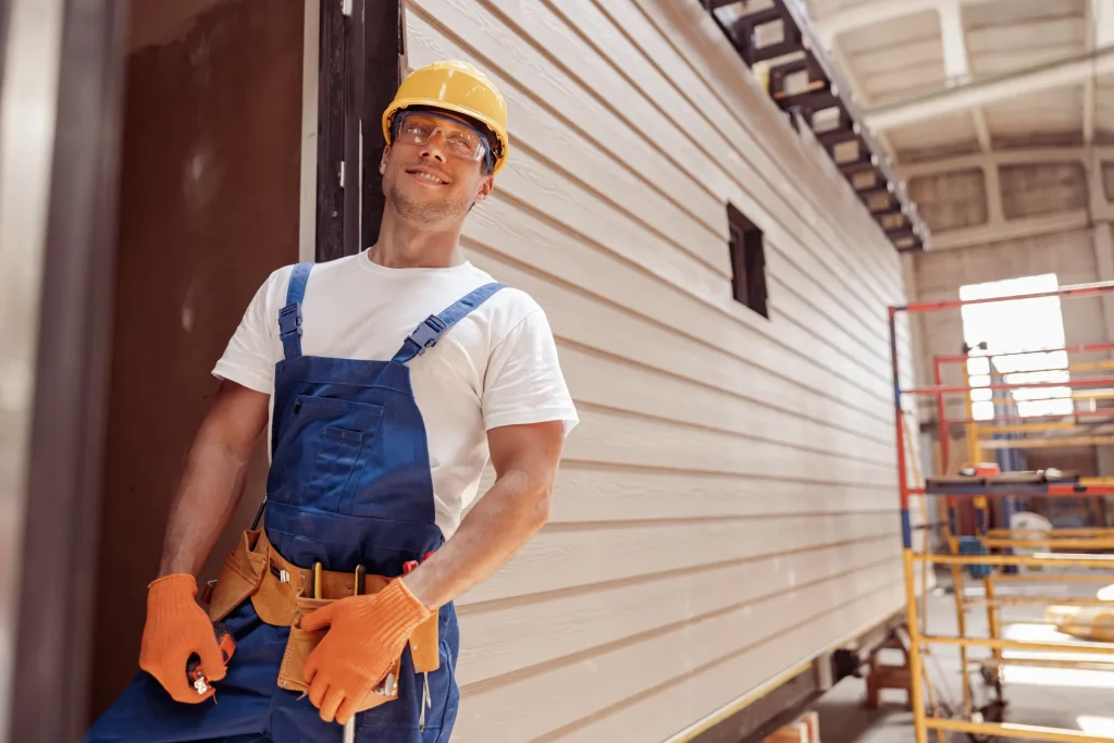 Artisan souriant sur un chantier de volet roulant sur la Côte d’Azur, casque et gants de travail