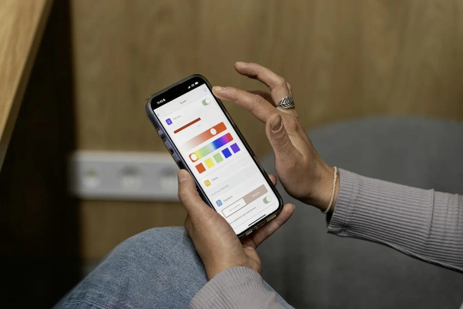 Mains tenant un smartphone affichant une application de maison connectée, dans un intérieur en bois