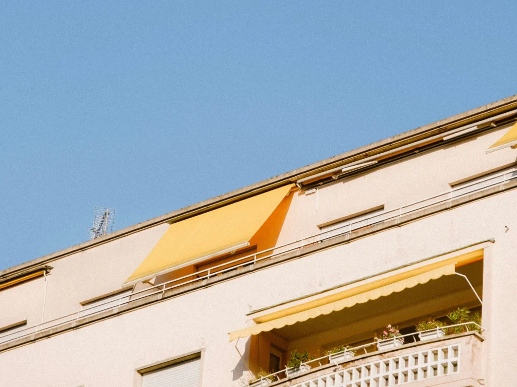 Store banne jaune déployé sur le balcon d’un immeuble, ciel bleu – stores extérieurs à Saint-Laurent-du-Var