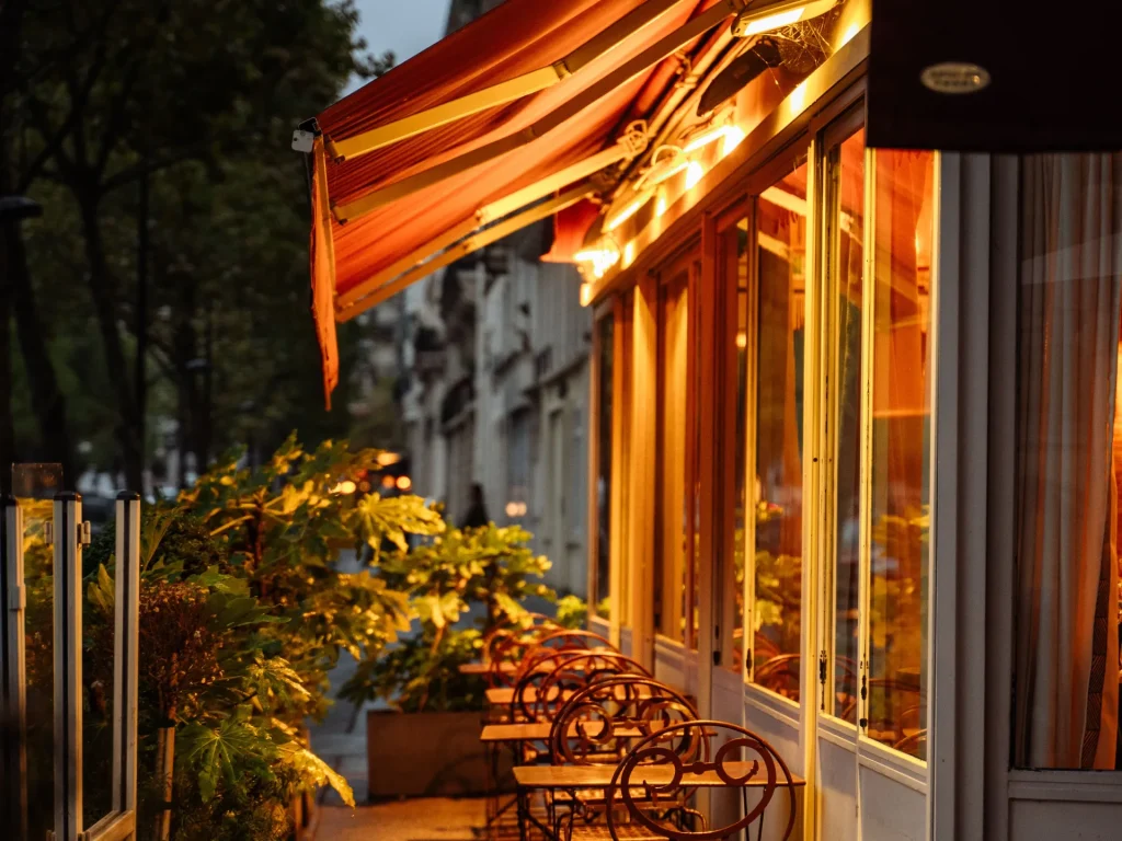 Terrasse de café éclairée le soir sous un store banne orange – stores extérieurs à Vallauris