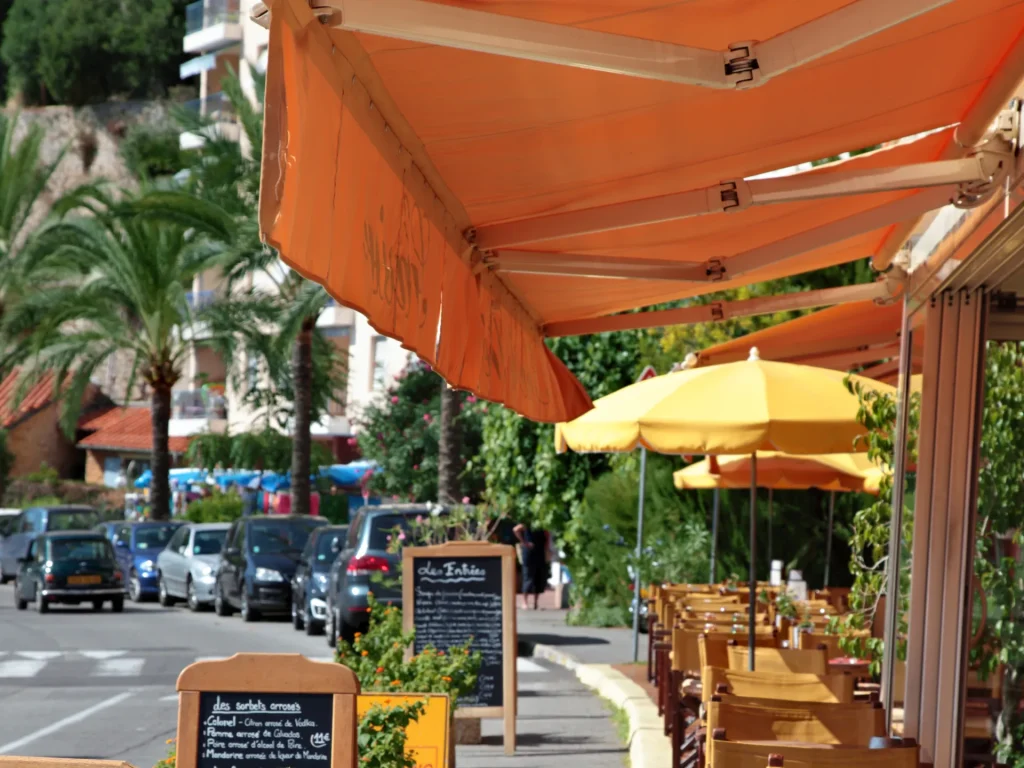 Terrasse de restaurant abritée par un store banne orange, palmiers en arrière-plan – remplacement toile store banne