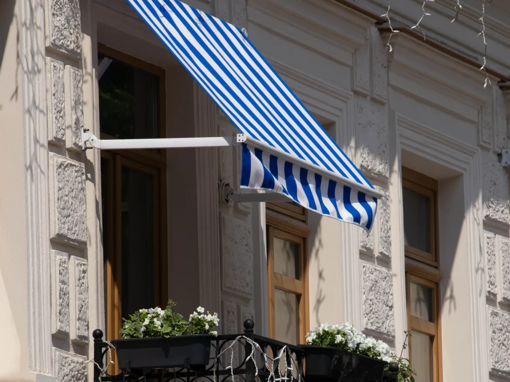 Store rayé bleu et blanc au-dessus d’un balcon en fer forgé – volet roulant copropriété