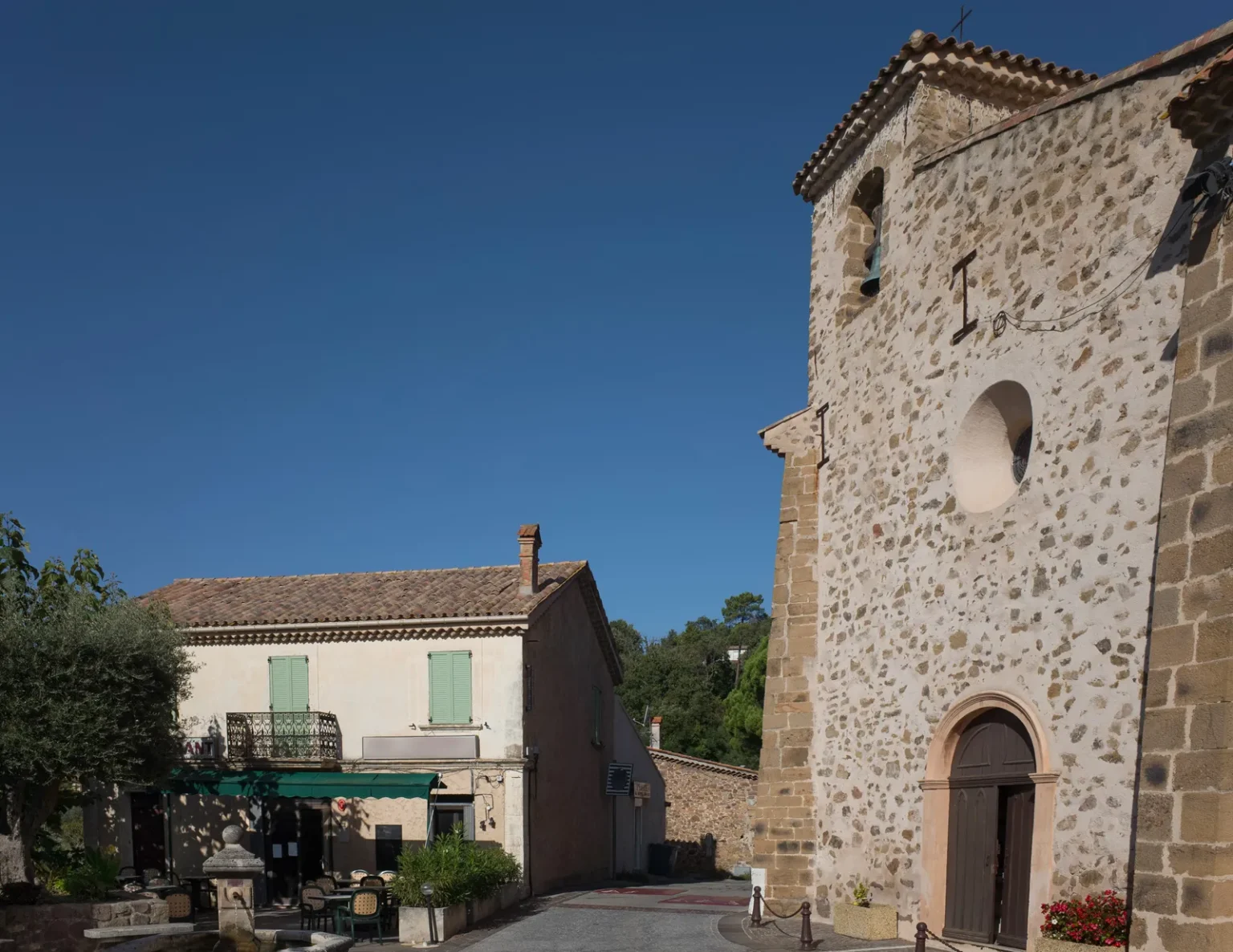 La place de l'église des Adrets-de-l'Estérel et sa façade en pierre sous un ciel bleu